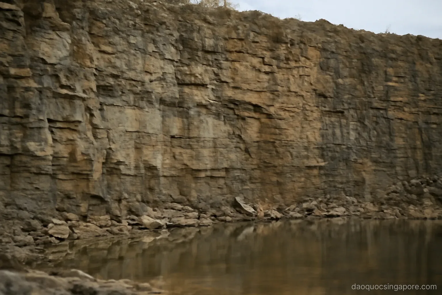 an exposed rock face in a disused quarry with layered stone and pooled water below